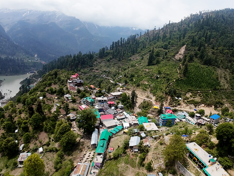 “Tosh Village in Himachal surrounded by snow-capped peaks and pine trees”